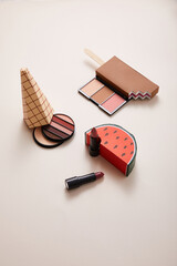 Wall Mural - powder with eyeshadows and decorative ice-cream with lipsticks on beige background, close view, beauty concept 