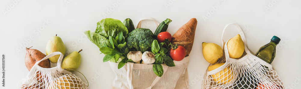 Online grocery healthy shopping. Flat-lay of fruit, vegetables, greens, bread and oil in eco-friendly bag over white background, top view, wide composition. Shop online during pandemic of coronavirus - obrazy, fototapety, plakaty 
