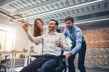 Wall Mural - Happy co-workers racing on chairs in modern office