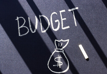 the word budget is written in white chalk on a black surface and a bag of money