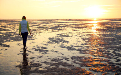 A young woman walks over the tidal mudflats of the Waddensea at low tide, Holland