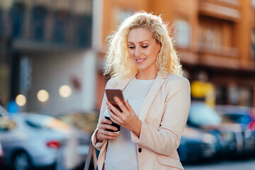 Happy business woman using smartphone on the street