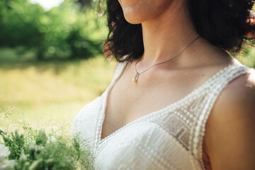 Wall Mural - Brunette bride in white wedding dress neckline close up. Necklace on the neck. Outdoor photo, wedding day concept.