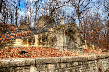 wide angle shot looking up at Pere Marquette Cross at the top of a set of stone steps on the side of a hill, tall leafless winter trees in the background with blue sky behind, Graftin Il 