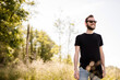 © _robbie_ - A young unshaven man in his 30s wearing dark shades and a black, round-neck shirt smiling, confident man with facial hair wearing dark shades blurred background.