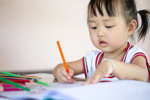 A Young Asian Female Toddler With Black Hair Is Smiling. She Happily With Colored Pencils.And Copy Space.
