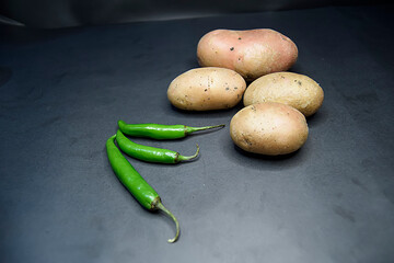 Selective focus of potatoes and green chillies on black background, Selective focus on green chillies and potatoes on black, cooking concept, food and drink.