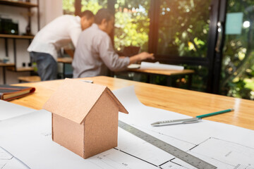 House model on desk over confident team of architects working together in a office. Architect discuss with engineer about project in office, architectural concept.