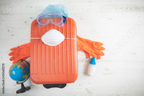 Cuadros en Lienzo Travel bag suitcase with earth globe, gloves, mask and head protection from viruses and flu influenza