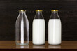 Three glass bottles. Two bottles with milk and one empty bottle on a wooden table.