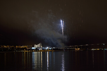 Beautiful firework on night sky in tromsoe city with bridge, cathedral and colorful reflection on the cold fjord water surface on new years eve