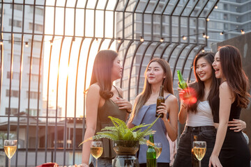 Wall Mural - Young beautiful group of Asian girl frinds holding beer bottle chatting and smiling together in party at rooftop on evening with lens flare and copy space