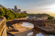 Biarritz, France. Panoramic view of the famous stone bridge to the Rocher du Basta, cityscape and coastline with sand beaches and port for small boats. Golden hour. Holidays in France.