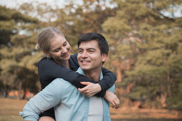 Young coupe in park. Boyfriend carrying his girlfriend on piggyback.