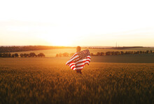 Beautiful Girl With American Flag In A Wheat Field At Sunset. 4th Of July.  Independence Day, Patriotic Holiday.