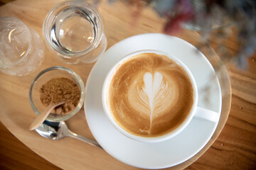 A cup of hot latte with latte art with sugar and a glass of water on wood table.