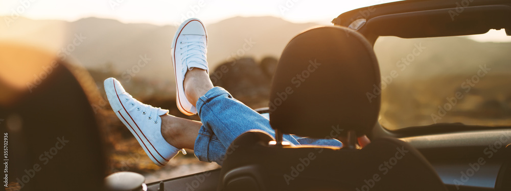 A young girl rests and pushes her shoes out of the convertible to enjoy the view - obrazy, fototapety, plakaty 