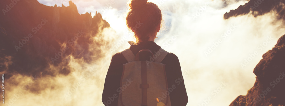 Traveling woman with a backpack standing on a cliff and enjoying landscape and sunset. - obrazy, fototapety, plakaty 