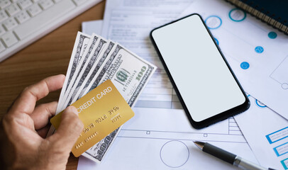 Wall Mural - Close-up of hand  businessman holding credit card and dollar with mobile phone and paperwork on desk