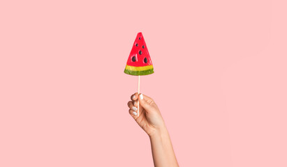 Wall Mural - Young girl showing watermelon lollipop on pink background, closeup of hand