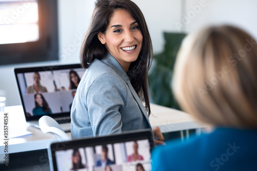 Fotomural Two business women speaking while doing a video call with diverse colleagues on online briefing with laptop in the office