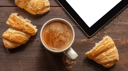 aromatic coffee, fresh croissants and a tablet on a wooden table