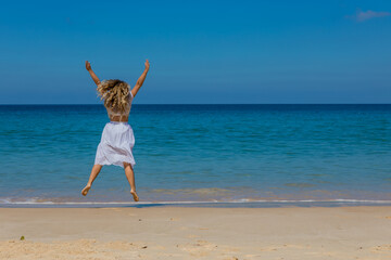 Wall Mural - Young beautiful girl in white clothes walks along the sandy beach near the water