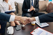 © DragonImages - Business people shaking hands over table with financial documents after closing deal