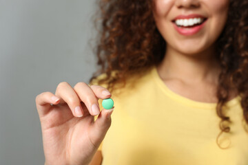 Wall Mural - African-American woman with vitamin pill on light grey background, closeup