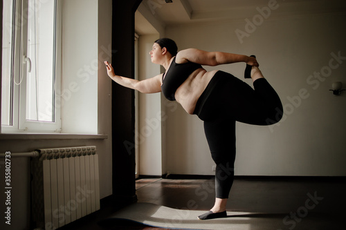 Overweight woman doing yoga exercise in living room. Yoga for weight loss, healthy lifestyle and home workout
