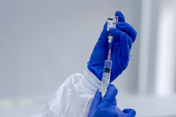 Scientist or researcher hand in blue gloves holding flu, measles, coronavirus, covid-19 vaccine disease preparing for human clinical trials vaccination shot, medicine and drug concept.