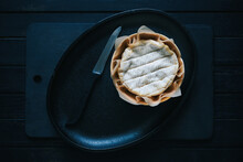 Round French Camembert Cheese In A Black Cast-iron Plate With Knife On A Black Table Top View 
