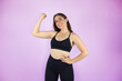 © Irene - Young beautiful woman standing over purple isolated background wearing sport chlotes and working out. Very happy, smailing and doing a gesture with his arm of strength and victory.