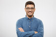 © Damir Khabirov - Young business guy wearing blue shirt and eyeglasses, standing with arms crossed, smiling happily and feeling confident, isolated on gray background