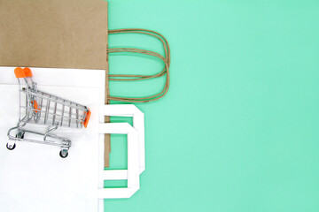 Small metal shopping cart with Kraft paper bags. The concept of using eco bags isolated on a green background. Copy space. Flatly. The view from the top.