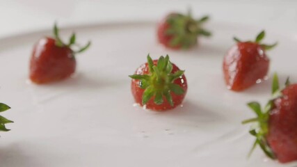 Wall Mural - Ripe red strawberry fruit falls into the center of a plate of water with splashes and drops of water. A few berries lie on the white plate. Slow motion. Full HD video, 240fps,1080p.