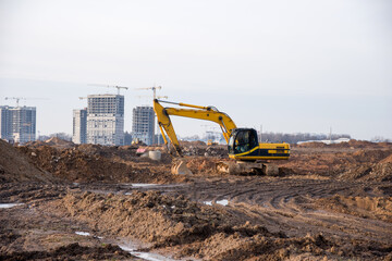 Excavator working at construction site. Backhoe digs ground for the foundation and for paving out sewer line. Construction machinery for excavating, loading, lifting and hauling of cargo on job sites