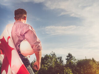 Young engineer, white hardhat and Canadian Flag in the park against the backdrop of green trees and the setting sun, looking into the distance. Close-up. Concept of labor and employment