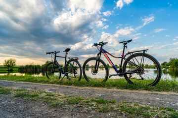 Leisure activity in nature with two mountain or touring bicycles equipped with luggage compartment near a lake with reflections of clouds and reeds at sunset. Beautiful blue sky above a country road.