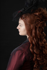 A young Victorian woman in a dark red and black ensemble against a black backdrop