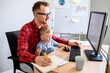 © Vadim Pastuh - Father works from home office while babysitting with toddler kid. Dad sits at the desk with a little son on his laps and typing on keyboard