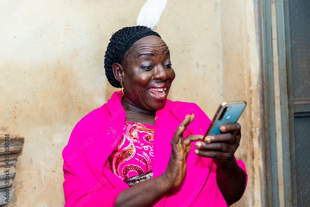 cheerful excited old black african woman receiving some good news with her smart phone.happy senior lady using mobile phone - obrazy, fototapety, plakaty 