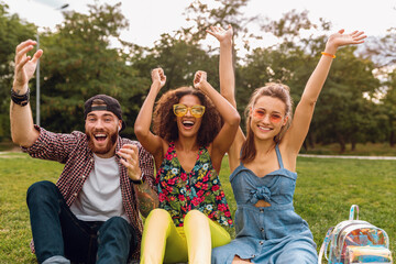 Wall Mural - happy young company of smiling friends sitting park on grass, man and women having fun together, colorful summer hipster fashion style, traveling sightseeing