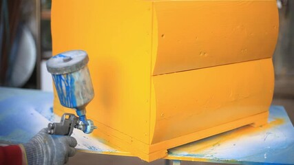 Wall Mural - Spray paint to the surface. Painting the hive in yellow. Work in the workshop. The spray gun with paint is aimed at a wooden box. Drawing an even layer.