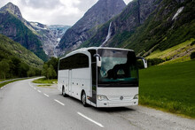 Trip To Norway. Blue Ice Tongue Of Jostedal Glacier Melts From The Giant Rocky Mountains Into The Green Valley With A Lot Of Waterfalls. Big White Tourist Bus Rides On The Road