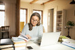 © shurkin_son - Serious gray haired female teacher in her sixties sitting at desk surrounded with textbooks, making lesson plan using laptop. Middle aged woman working distantly from home, holding open book