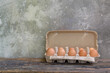 raw chicken eggs in egg box on the old wooden table with cement walls background.