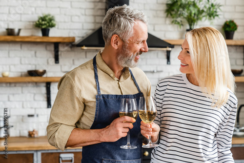 Fotografía Happy senior couple drinking wine at kitchen while cooking