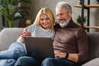 © InsideCreativeHouse - Beautiful middle aged couple using laptop and smiling while resting on couch at home