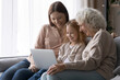 © fizkes - Smiling three generations of women relax on sofa in living room watch video movie on laptop, happy little girl with mom and senior grandmother rest on couch at home using modern computer together